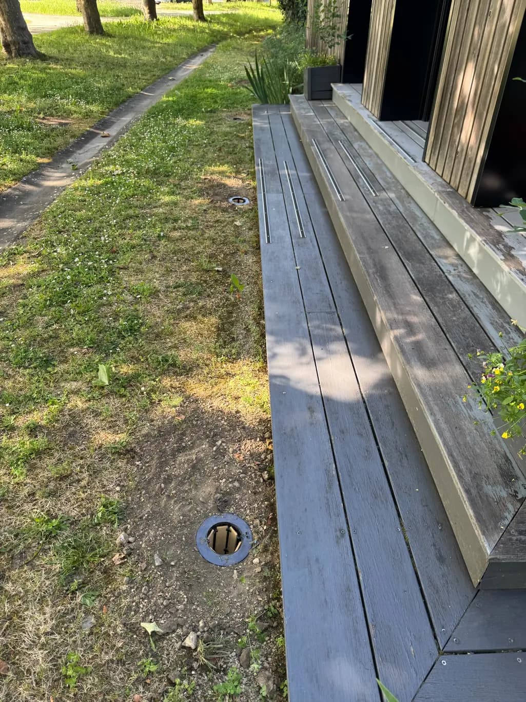 Station de piégeage de termites enterrée à fleur de terre devant une terrasse en bois à Créon