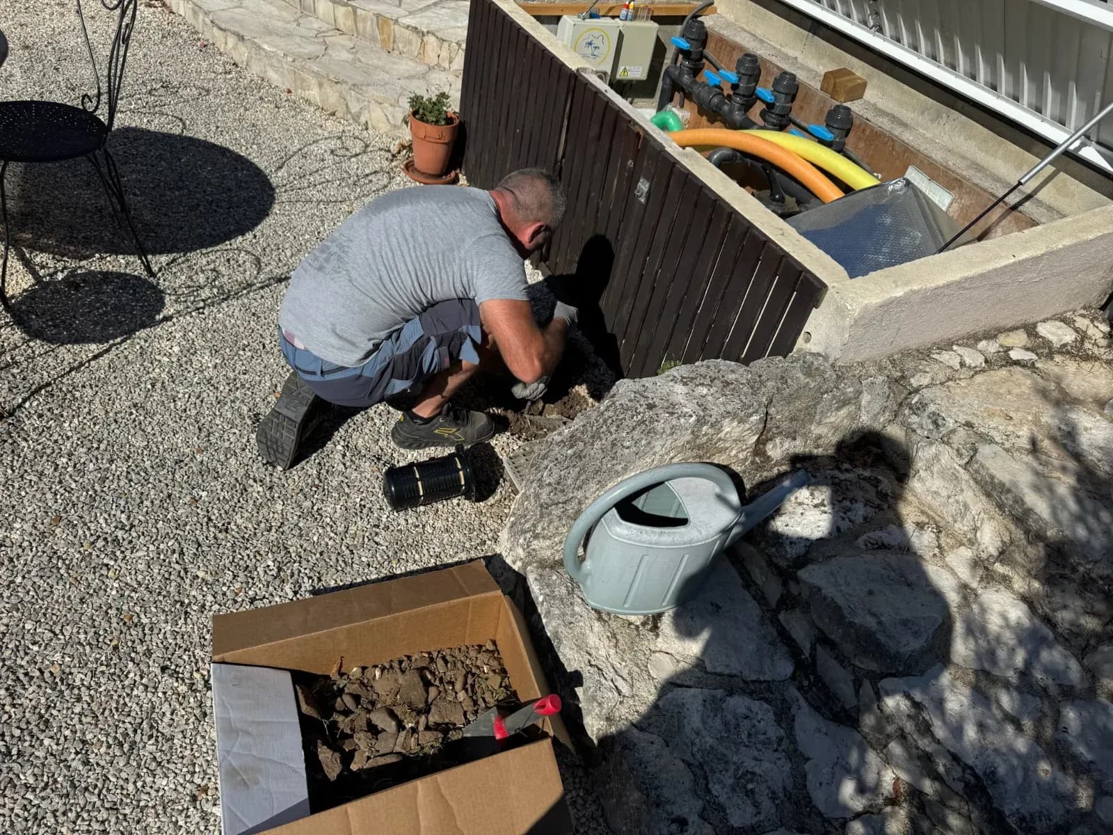 Technicien accroupi creusant l'emplacement d'une station d'appâtage contre un mur en pierre à Port-Sainte-Foy-et-Ponchapt