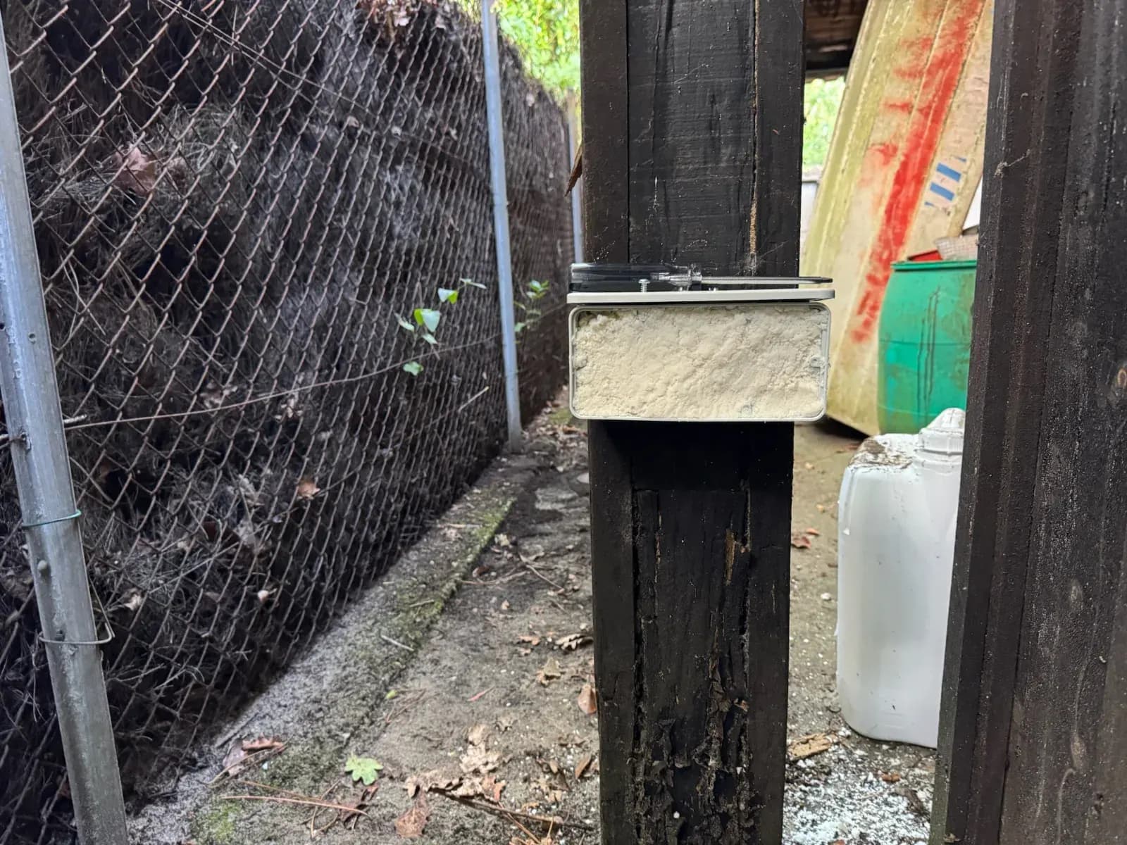 Boîtier d'appâtage anti-termites fixé sur un poteau bois noirci et dégradé d'une dépendance à Lège-Cap-Ferret