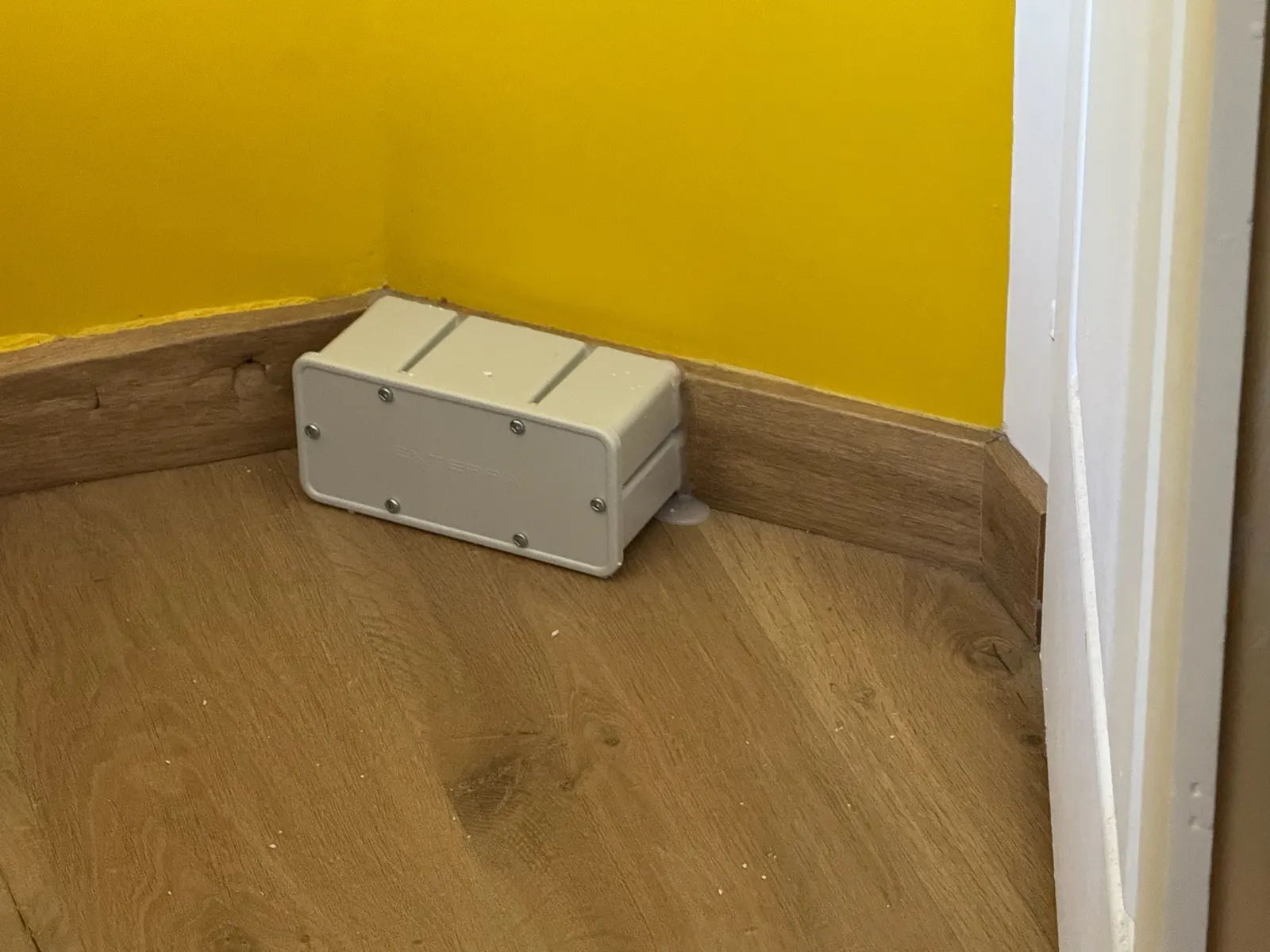 Station d'appâtage Exterra™ d'intérieur posée contre une plinthe dans une maison à Pessac