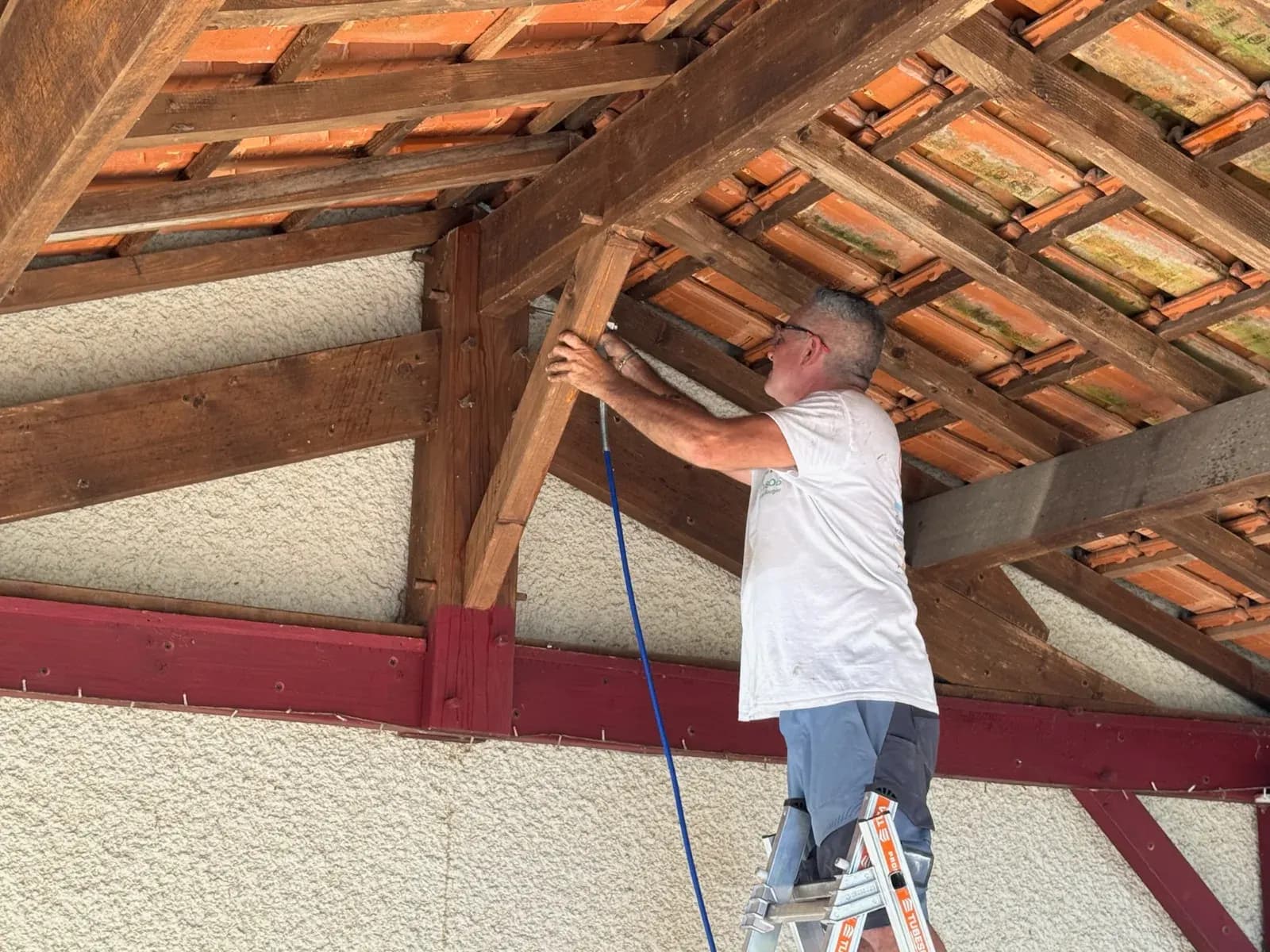 Applicateur traitant au pistolet un poteau de charpente en bois sous le carport à Saint-Selve